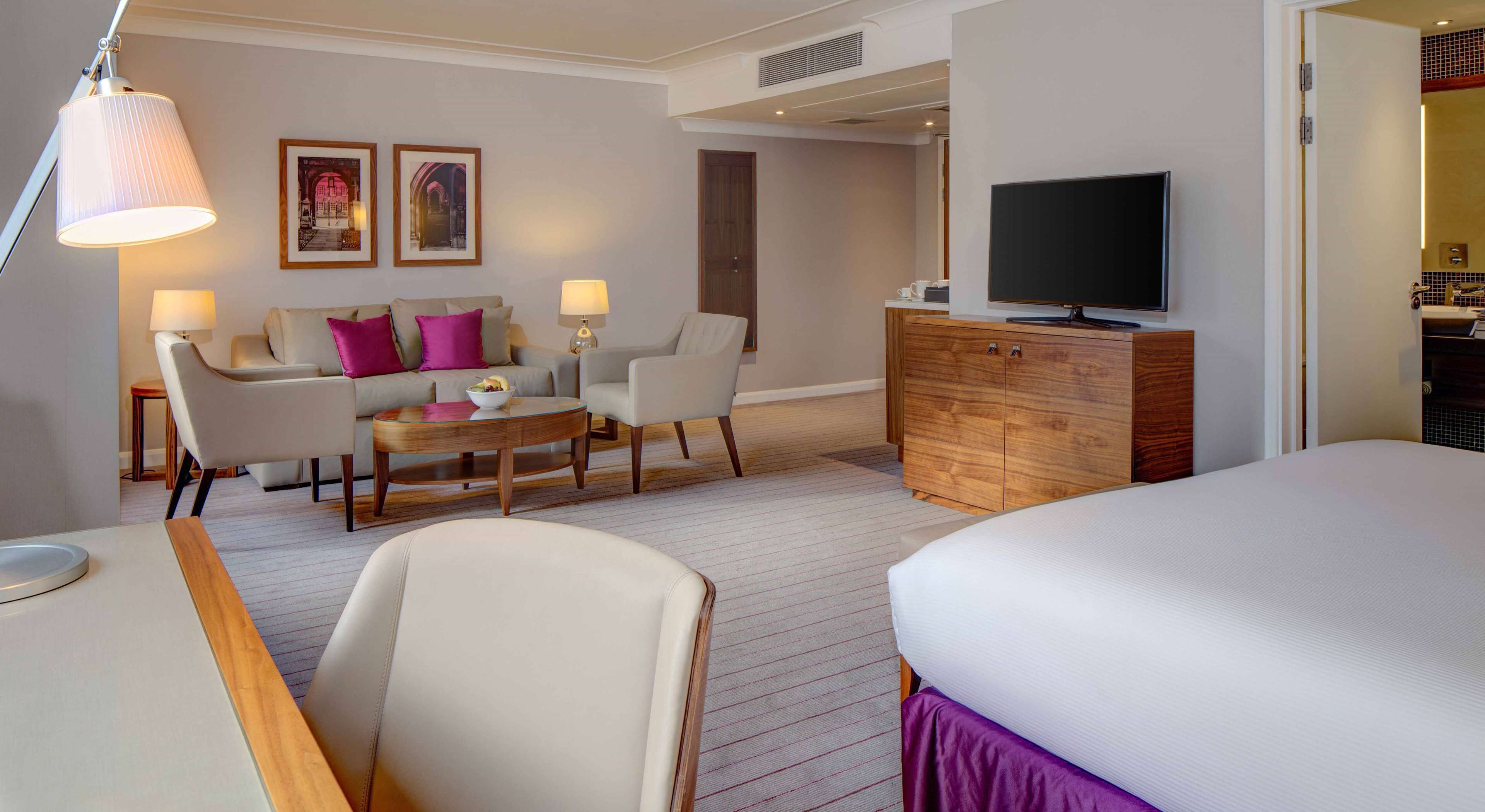 Una habitación de hotel con cama, televisor, escritorio, silla, sofá y una mesita.
