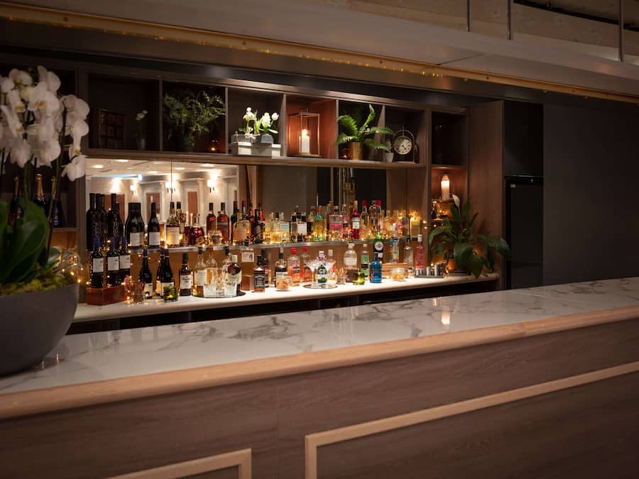 A bar area with shelves of liquor bottles, a marble countertop, and decorative plants.