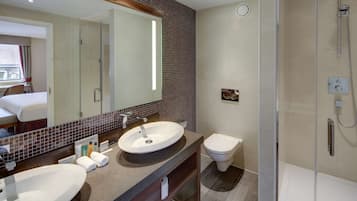 A modern bathroom with a large mirror, two sinks, a toilet, and a shower.