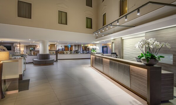 A spacious lobby with a reception desk, seating area, and a modern kitchen in the background. - Hilton Cambridge City Centre (Cambridge)
