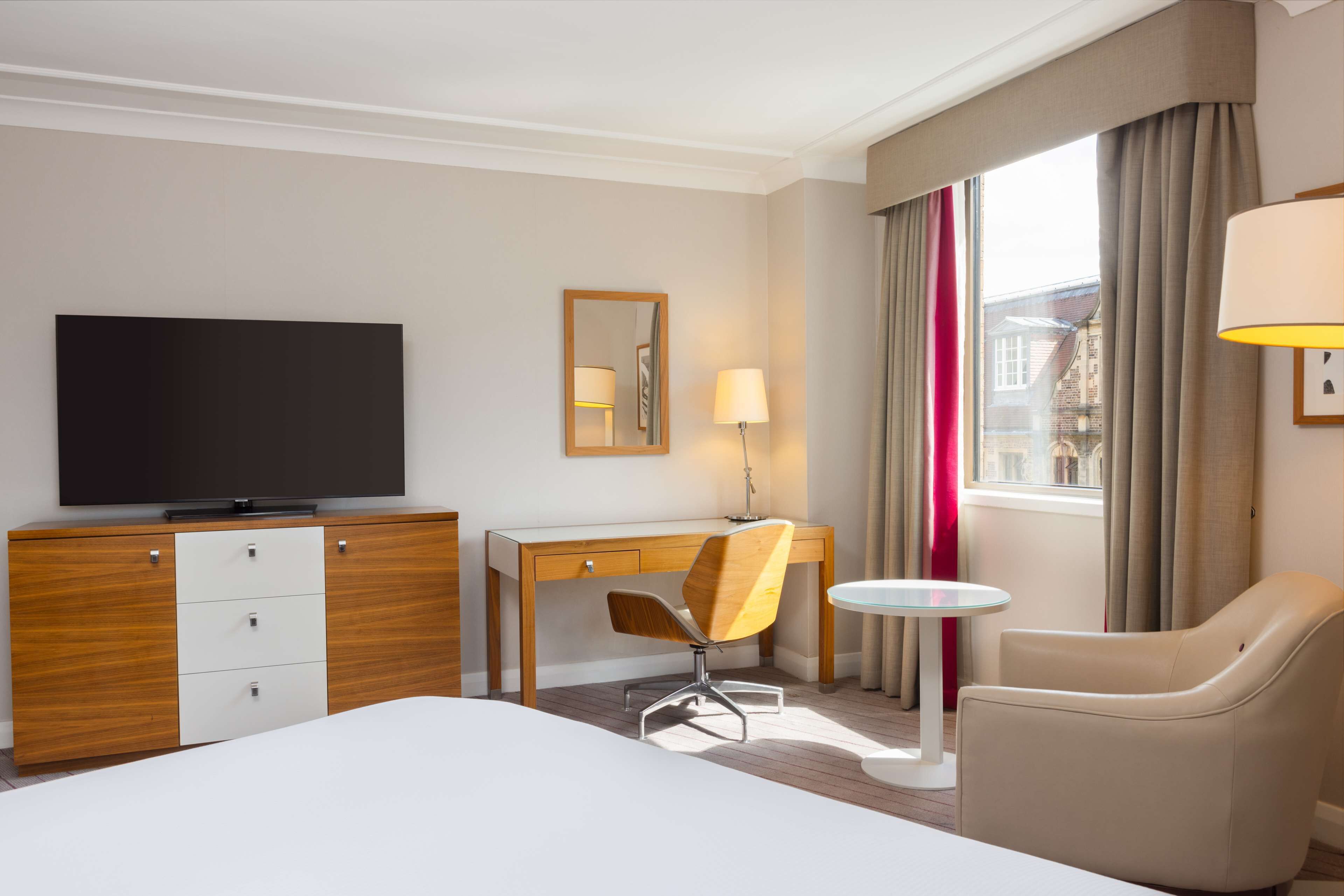 Ein Hotelzimmer mit Bett, Schreibtisch, Stuhl, Fernseher und einem Fenster mit Vorhängen.