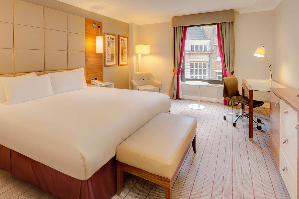 Una habitación de hotel con una cama grande, un escritorio, una silla, una mesita y una ventana con cortinas.