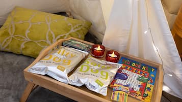 Una bandeja de madera con aperitivos, una vela y un libro para colorear sobre una cama.