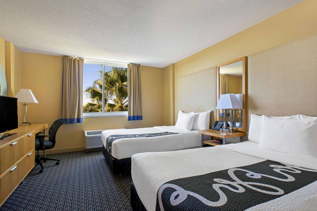 Ein Hotelzimmer mit zwei Betten, einem Schreibtisch, einem Fernseher und einem Vorhangfenster.