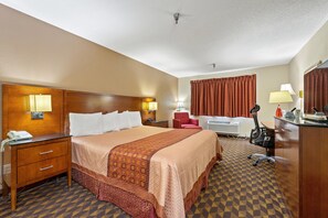 A hotel room with a large bed, a desk, a chair, a telephone, and a lamp.