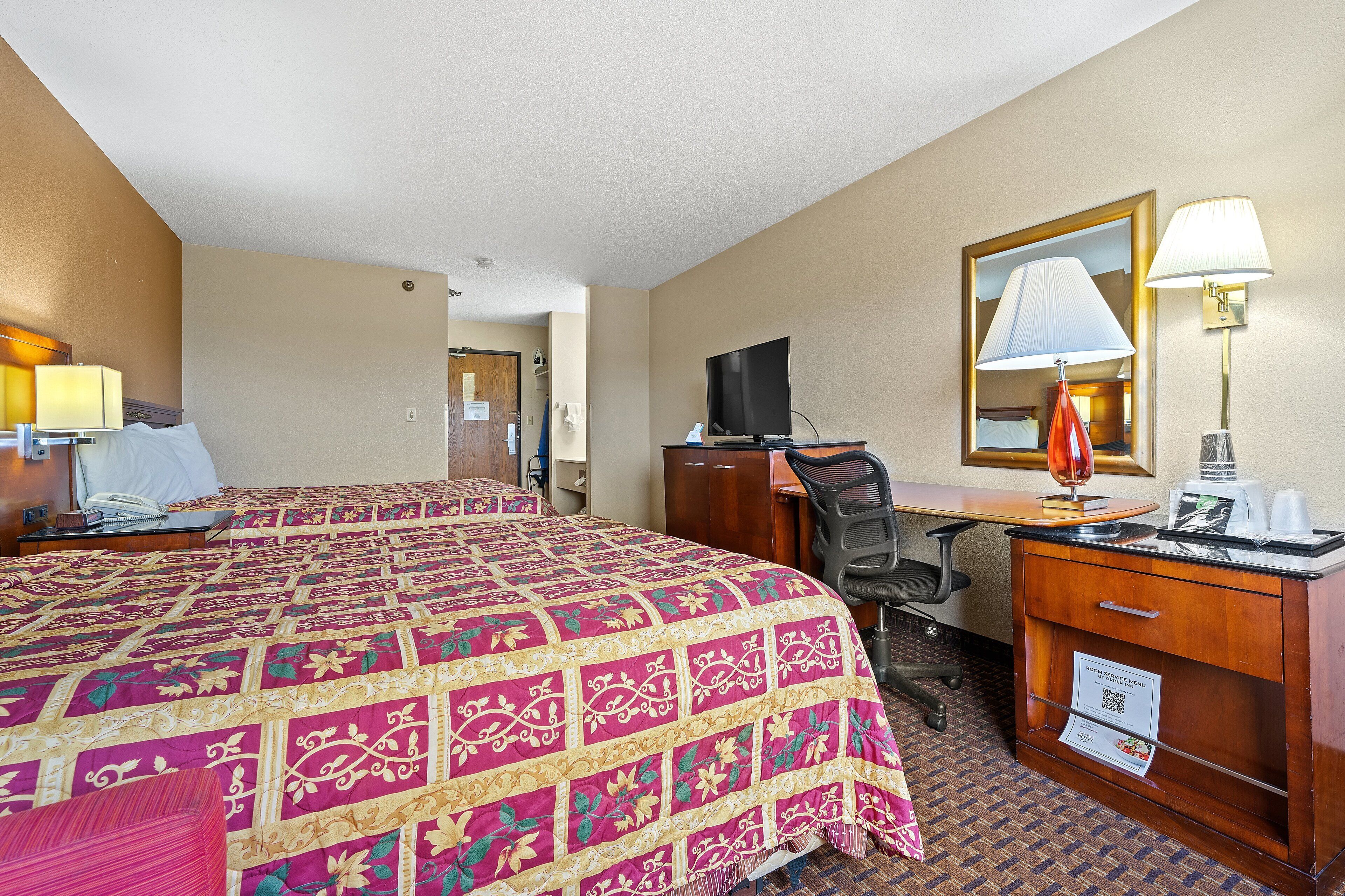 A hotel room with a large bed, a desk, a chair, a television, and a desk lamp.