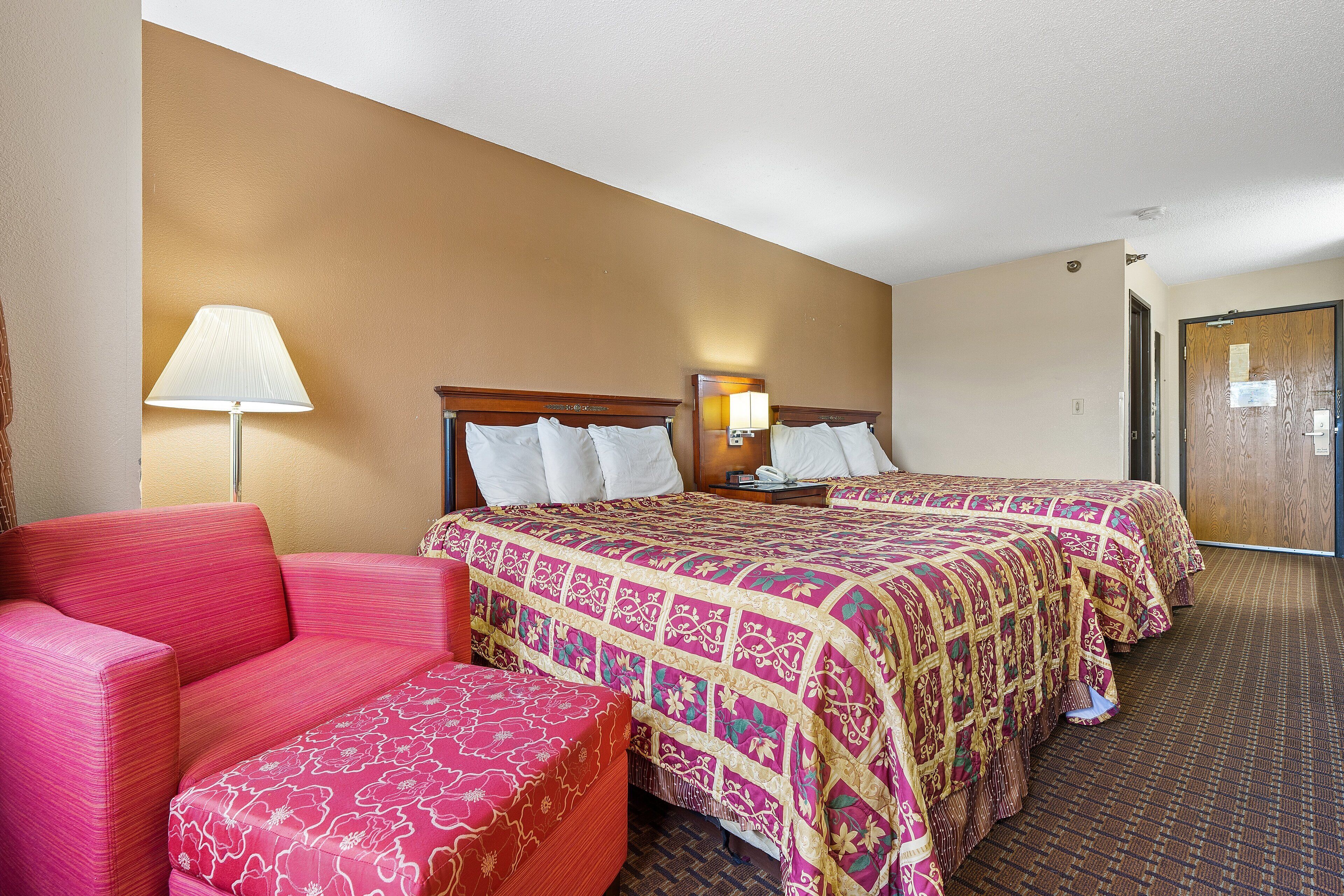 A hotel room with two beds, a sofa, a lamp, and a carpeted floor.