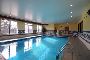 An indoor swimming pool with clear blue water, a tiled floor, and a pool ladder. - Geneva Motel Inn (St. Charles)
