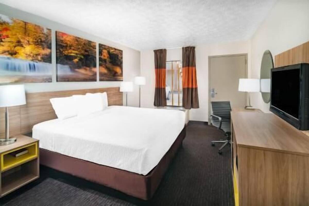 Ein Hotelzimmer mit einem Bett, zwei Nachttischen, einem Schreibtisch mit Stuhl, einem Fernseher und Bildern an der Wand.