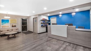 Un área de recepción con suelo de madera, mostrador de recepción, pared de acento azul y zona de estar con sofá y mesa de centro.