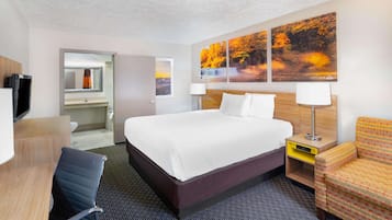 Une chambre d’hôtel avec un grand lit, un bureau avec une chaise, une télévision, une salle de bain et un mur décoré d’œuvres d’art sur le thème de l’automne.