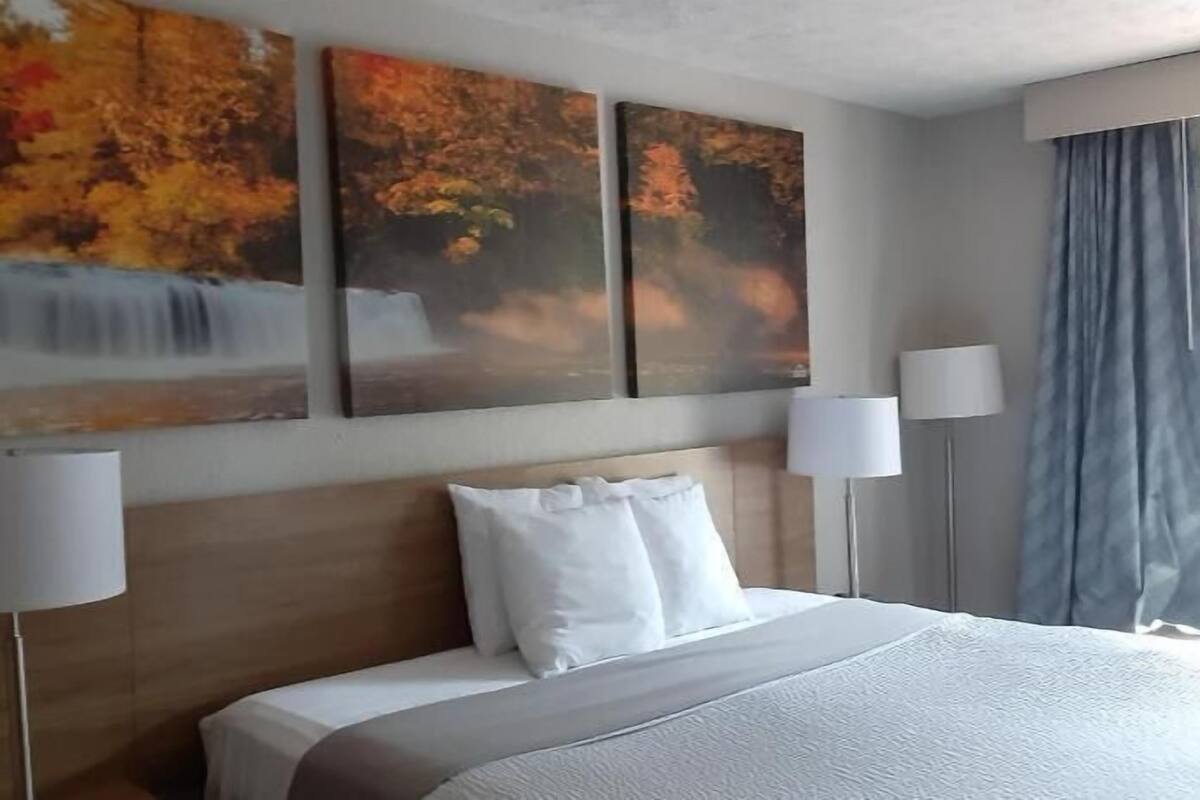 Ein Hotelzimmer mit einem großen Bett, zwei Nachttischlampen und drei herbstlich gestalteten Bildern an der Wand.