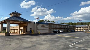 Un motel con entrada cubierta, una bandera y un estacionamiento.