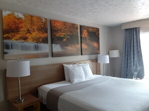 Habitación de hotel con una cama grande, dos lámparas de noche, una mesita de noche y tres cuadros con motivos otoñales en la pared.
