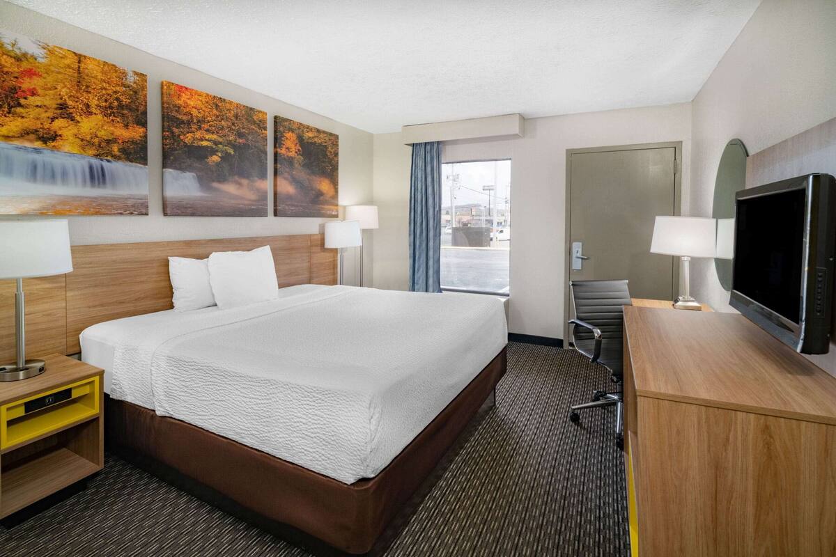 Ein Hotelzimmer mit einem großen Bett, einem Schreibtisch mit Fernseher und drei Bildern an der Wand.