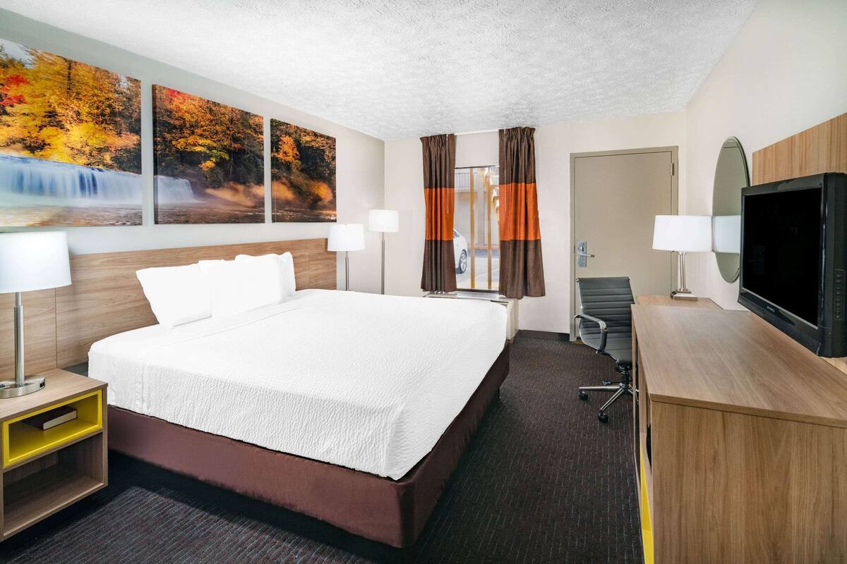 Ein Hotelzimmer mit einem großen Bett, einem Schreibtisch mit Fernseher und drei Bildern an der Wand.