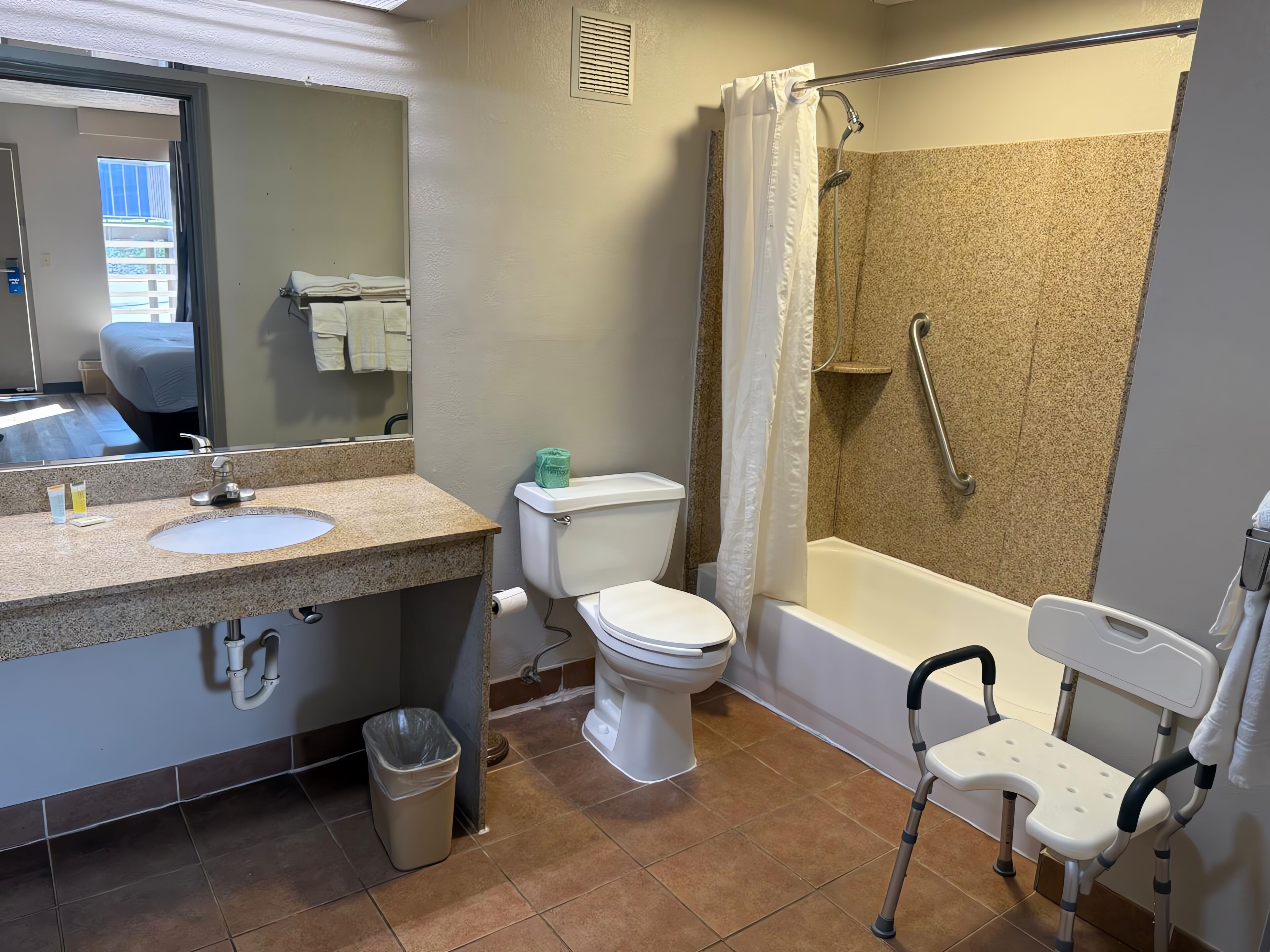 A bathroom with a sink, toilet, shower, and a wheelchair.