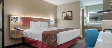 Ein Hotelzimmer mit einem Bett, Nachttisch, Lampe, Stuhl und einem großen Spiegel.