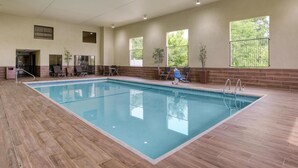 Una piscina interior con suelo de baldosas, algunas tumbonas y vistas a árboles a través de amplias ventanas.