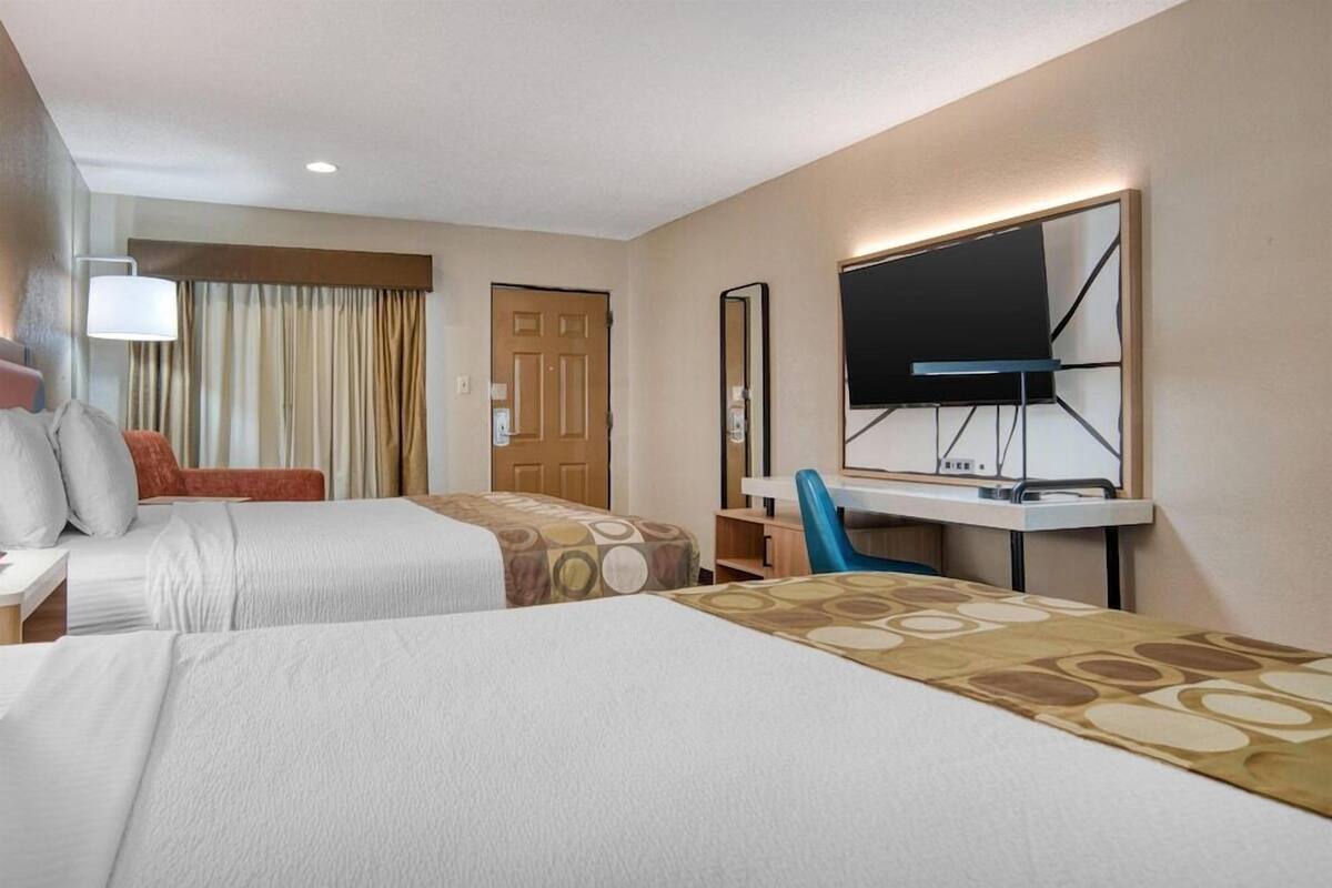 A hotel room with two beds, a desk, a chair, a TV, and a window with curtains.