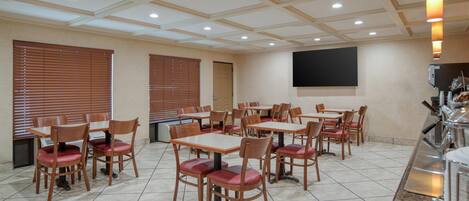 A conference room with multiple tables and chairs, a flat-screen TV mounted on the wall, and a coffee machine on the counter.