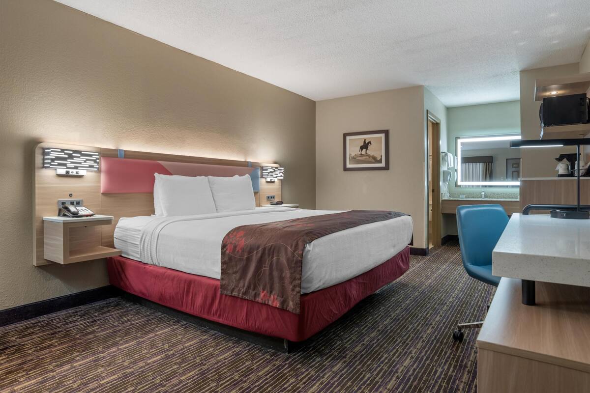 Een hotelkamer met een bed, nachtkastje, lamp, stoel, bureau en een grote spiegel.