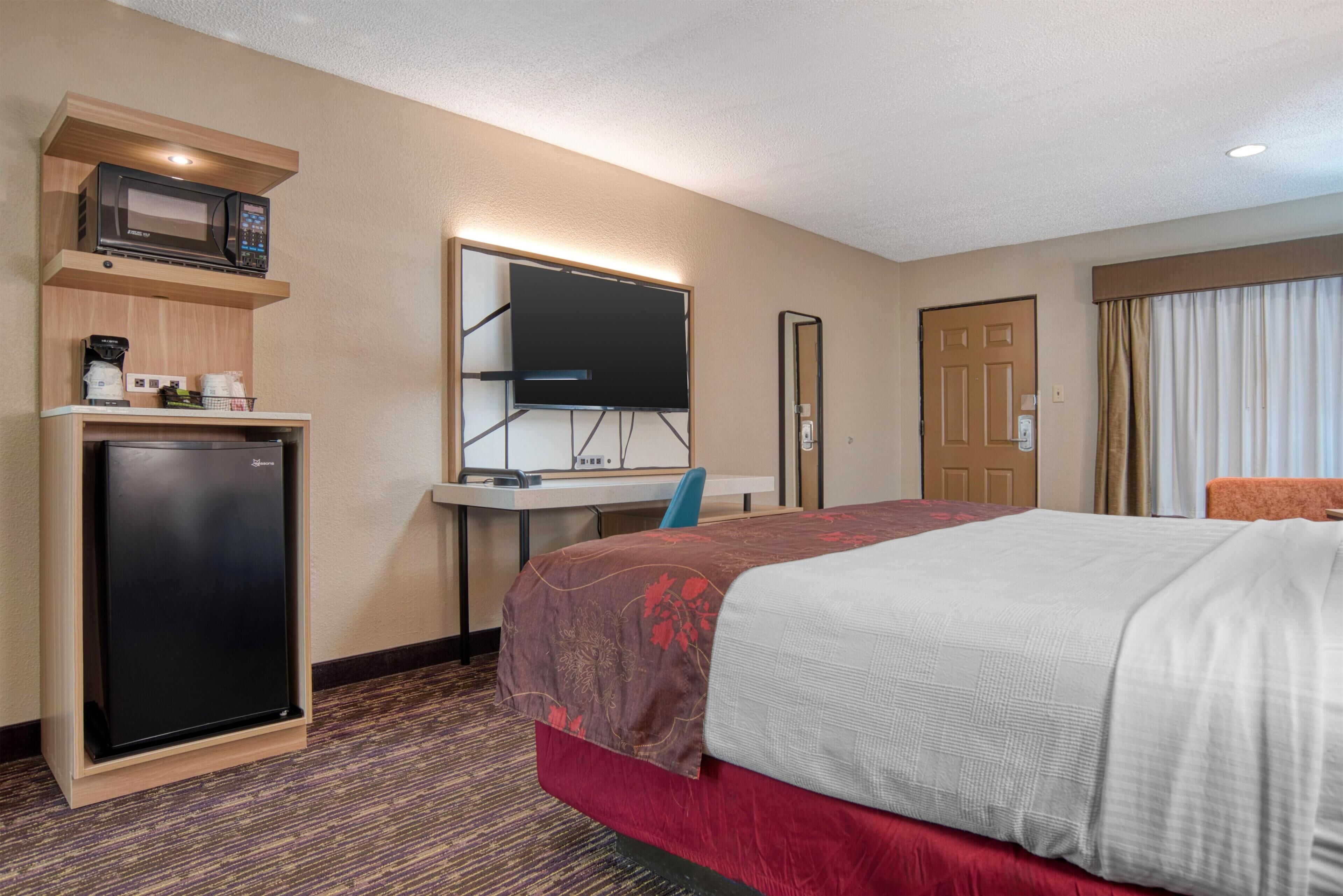 Quarto de hotel com cama, escrivaninha com computador, micro-ondas e frigorífico.