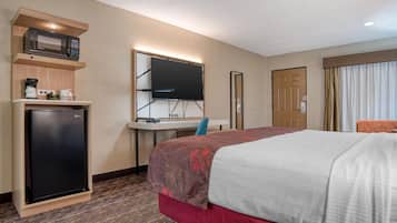 A hotel room with a bed, a desk with a computer, a microwave, and a refrigerator.