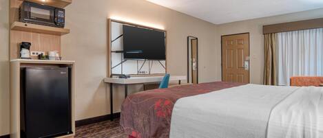 Quarto de hotel com cama, escrivaninha com computador, micro-ondas e frigorífico.