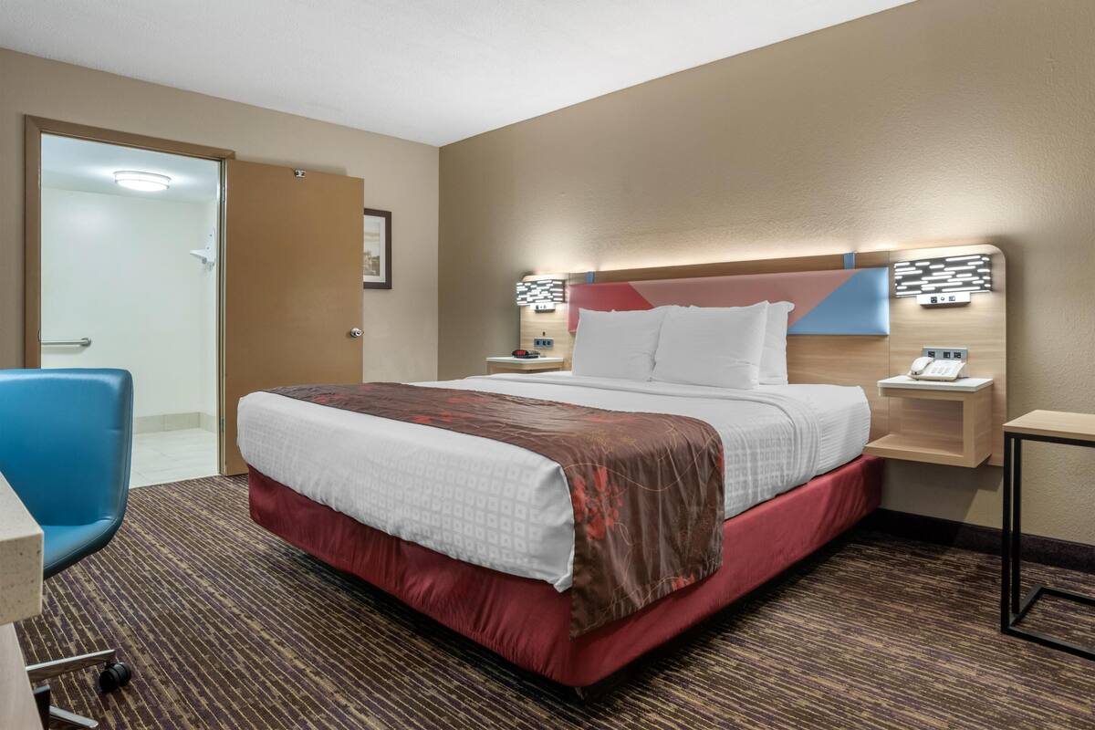 Een hotelkamer met een bed, een bureau, een stoel, een nachtkastje en een aan de muur bevestigde telefoon.