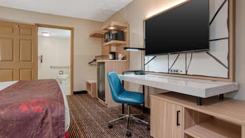 A hotel room with a bed, desk, chair, TV, microwave, and a small kitchenette.