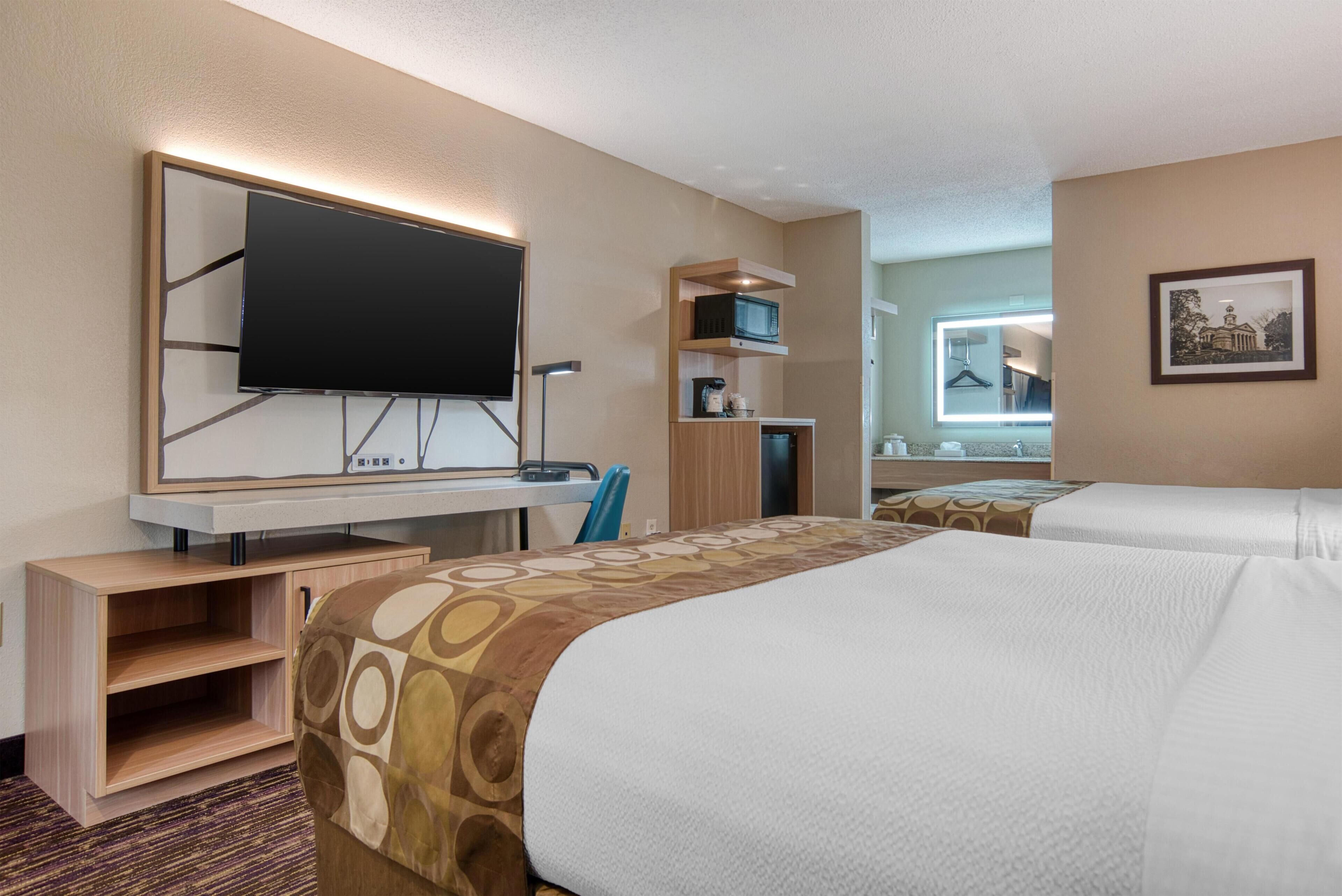 Ein Hotelzimmer mit einem Bett, einem Schreibtisch, einem Flachbildfernseher, einer Mikrowelle und einem kleinen Schrank.