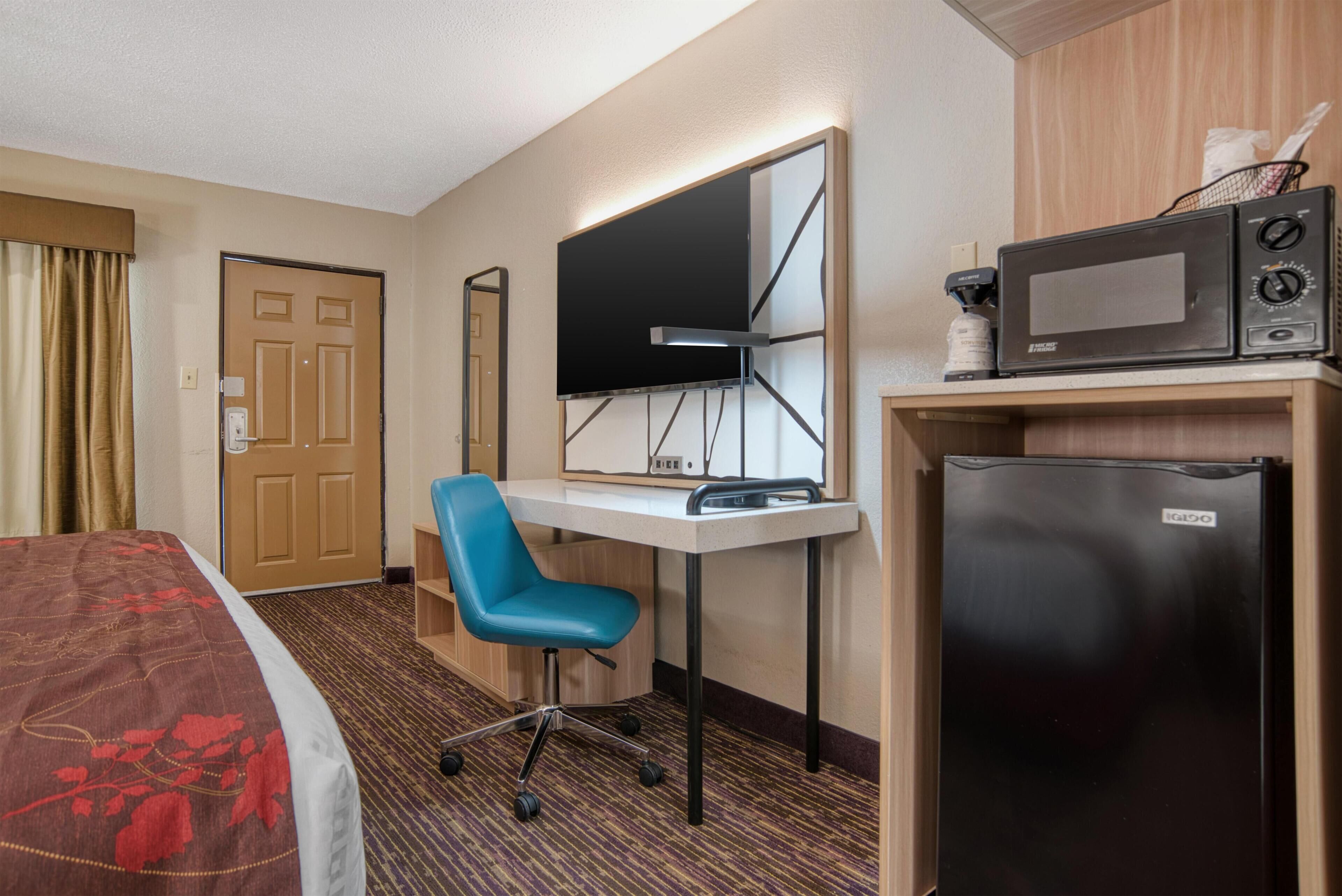 Ein Hotelzimmer mit einem Bett, einem Schreibtisch mit Stuhl, einem Flachbildfernseher, einer Mikrowelle und einem Kühlschrank.