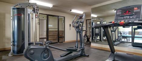 A gym with exercise equipment, a mirrored wall, and a door leading to another room.