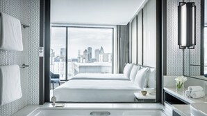 Een moderne hotelkamer met een groot bed, een badkuip, uitzicht op de stad en een badkamer met spiegel en handdoekhouder.