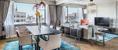 Una habitación de hotel moderna con comedor, sofá, televisión y vistas a la ciudad.