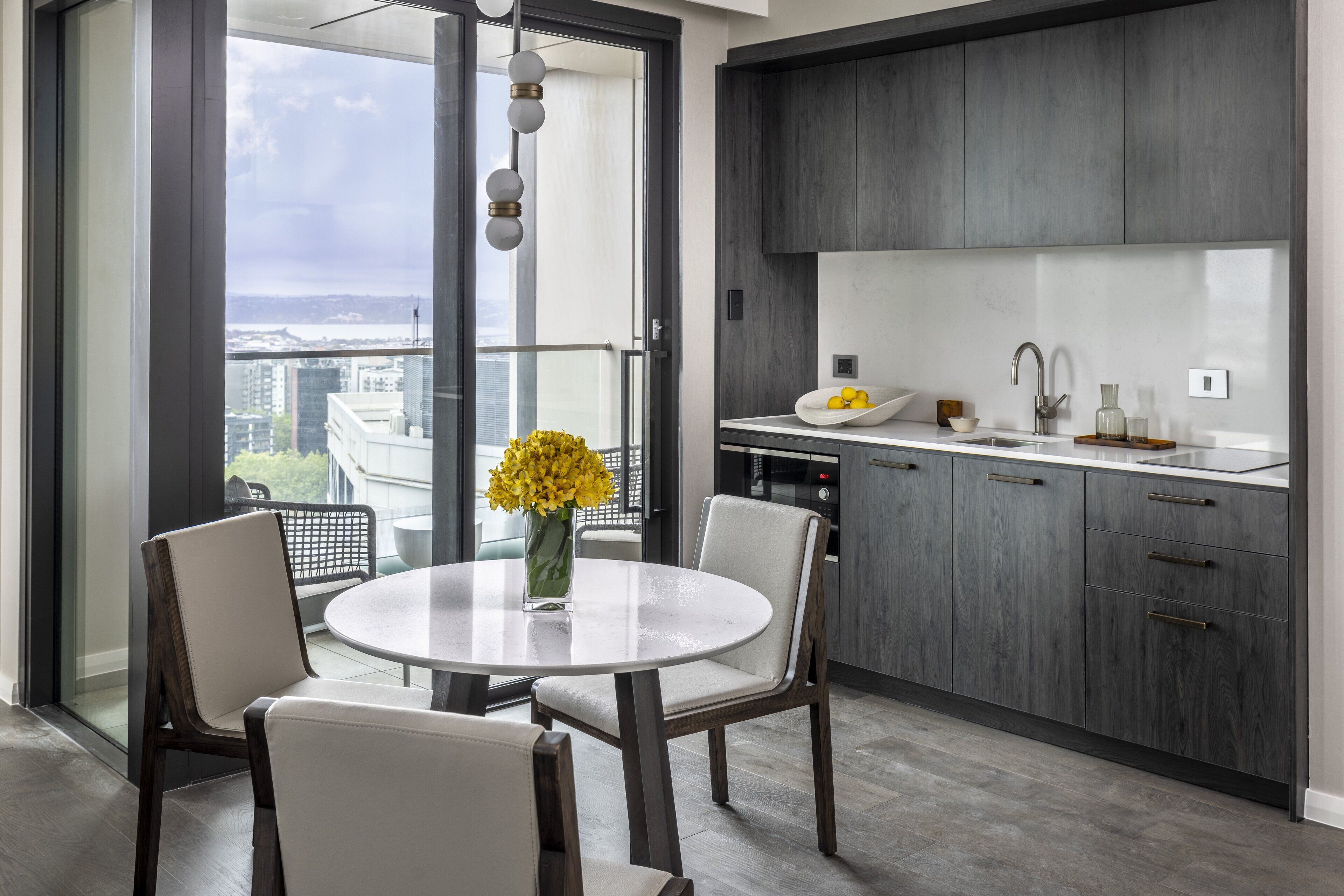 Una cocina moderna con una mesa redonda de comedor, sillas y vistas a la ciudad a través de amplios ventanales.