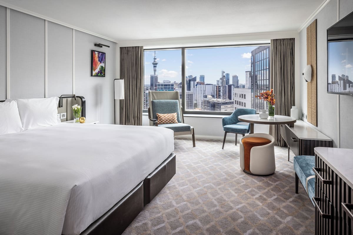 A hotel room with a large bed, a desk, a chair, and a view of the city skyline.