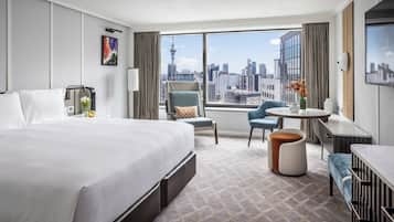 A hotel room with a large bed, a desk, a chair, and a view of the city skyline.