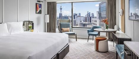 A hotel room with a large bed, a desk, a chair, and a view of the city skyline.