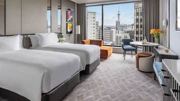 A hotel room with two beds, a seating area with a table and chairs, and a large window offering a city view.