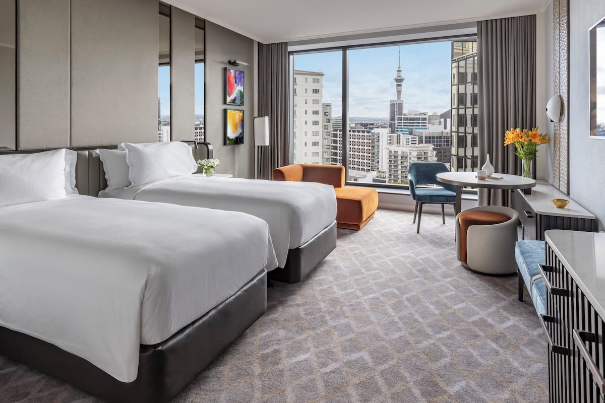 A hotel room with two beds, a desk, a chair, and a view of the cityscape.