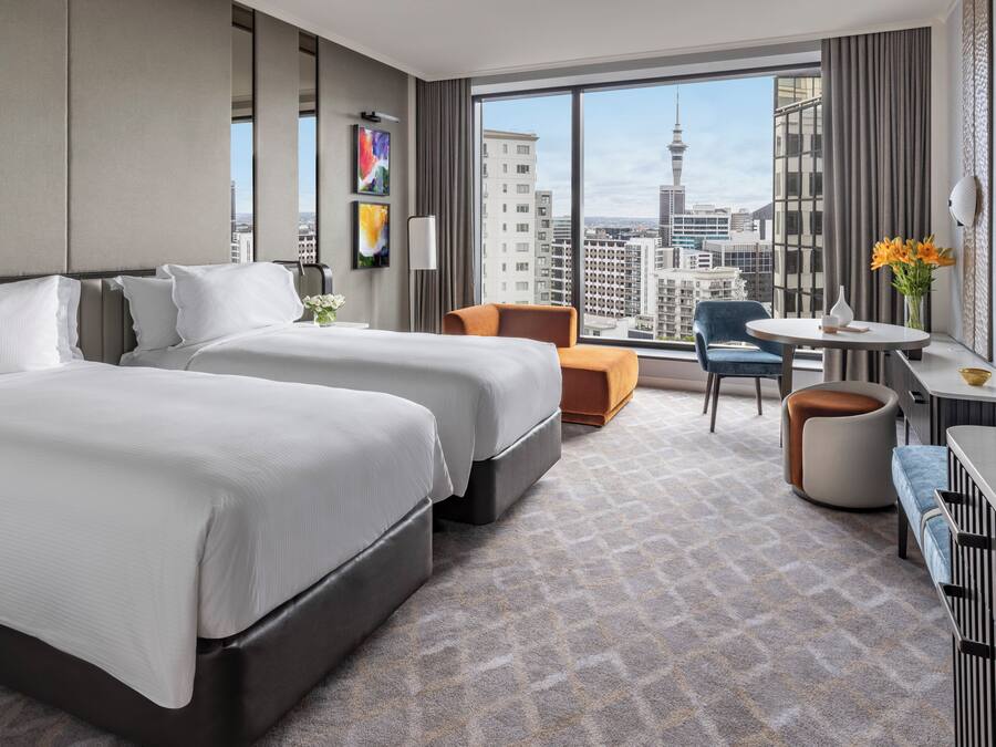 Quarto de hotel com duas camas, uma escrivaninha, uma cadeira e vista para a cidade.