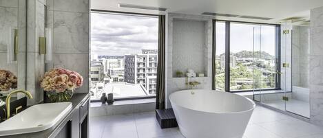 A modern bathroom with a freestanding bathtub, a large window with a city view, and a marble vanity.
