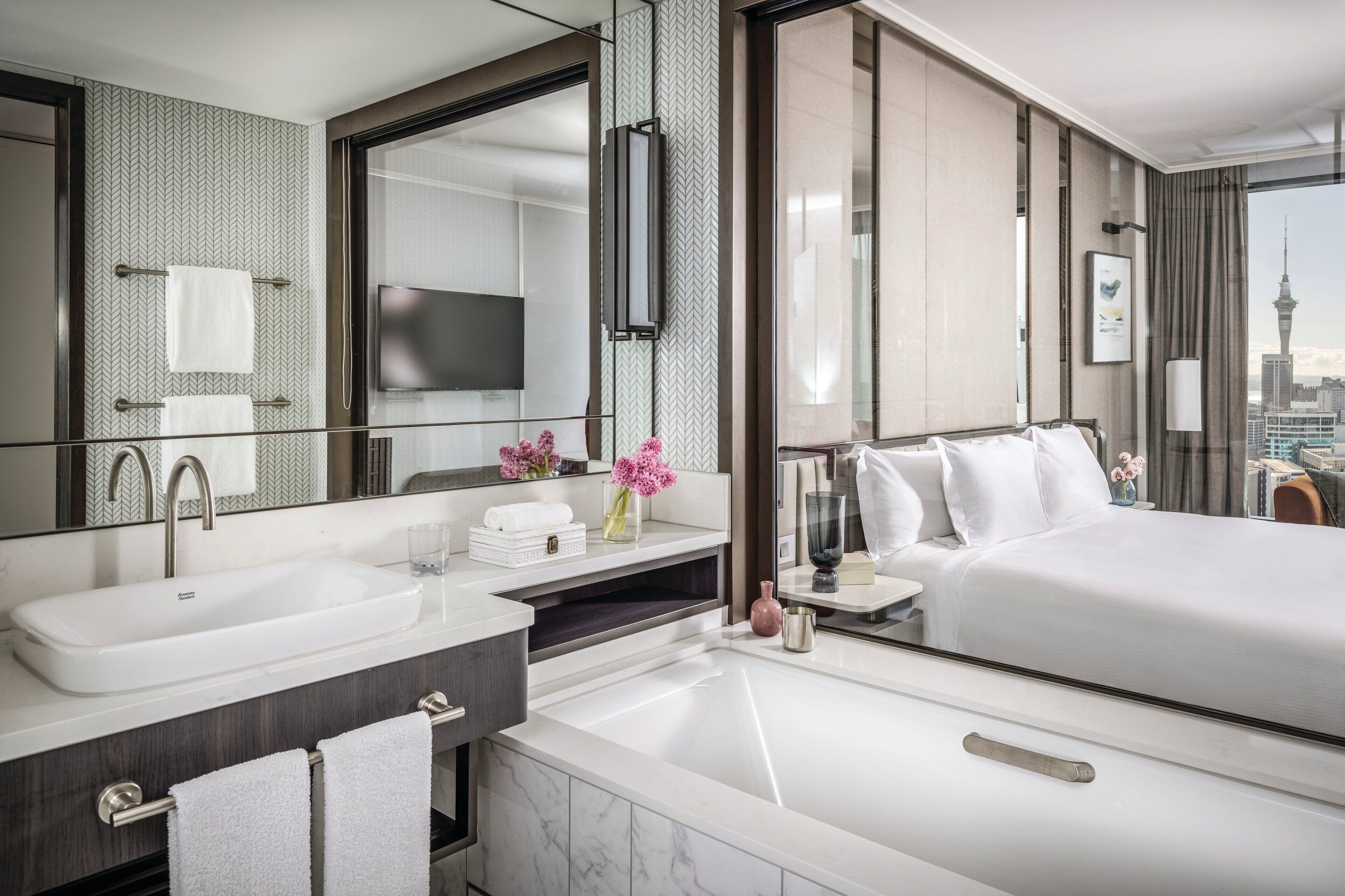 Een moderne hotelkamer met een groot bed, een badkamer met een wastafel en spiegel, en uitzicht op een stadsbeeld.