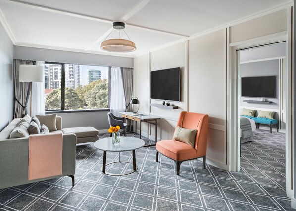 A modern hotel room with a sofa, armchair, desk, and TV.