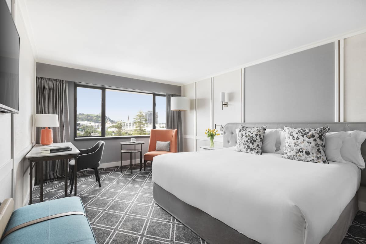 A hotel room with a large bed, a desk, a chair, and a view of the city.