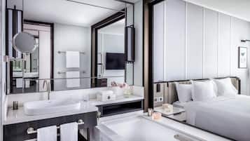 A modern hotel room with a large bed, a separate bathroom with a bathtub, a large mirror, and a flat-screen TV.