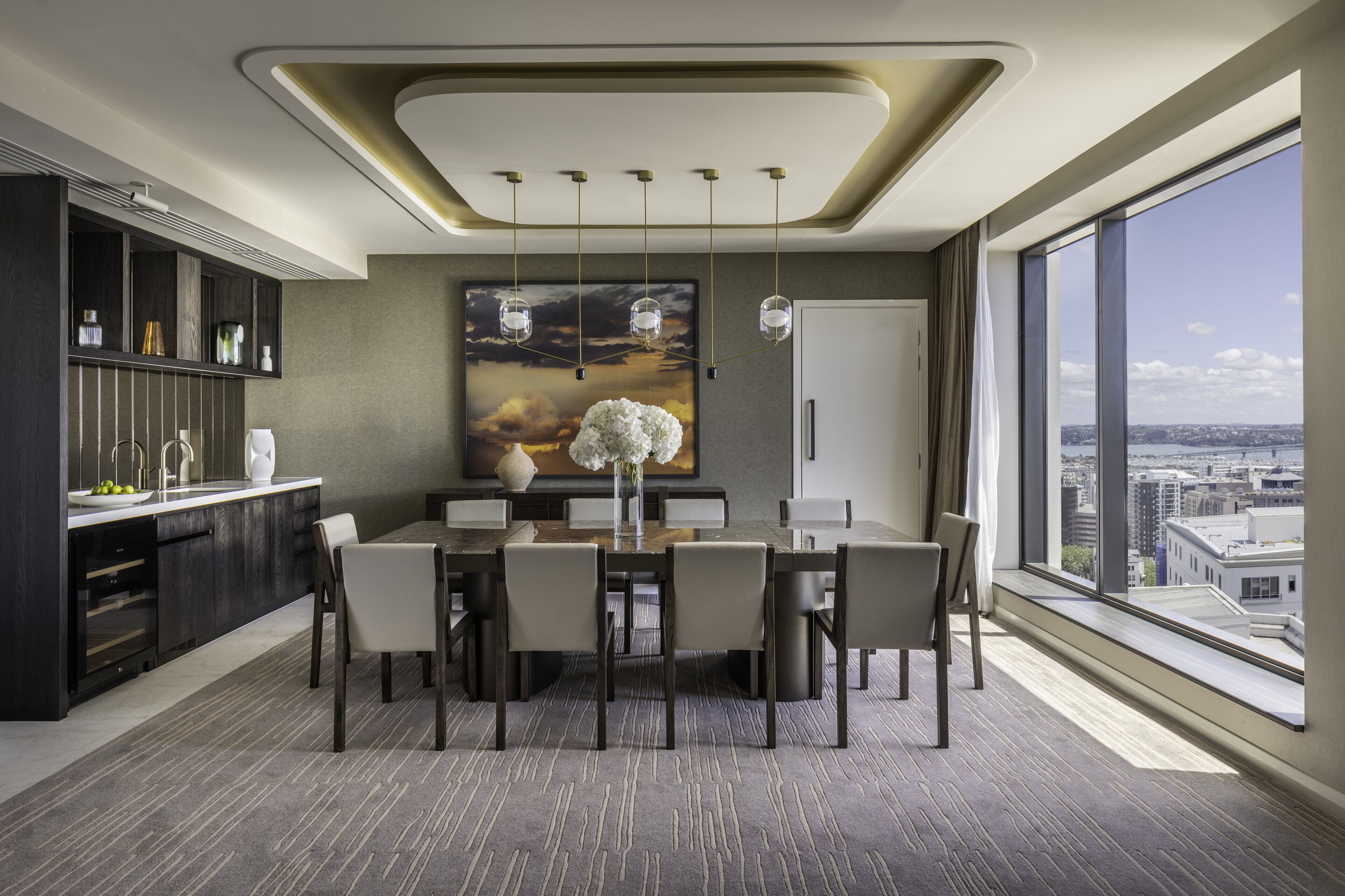 Uma sala de jantar moderna com uma mesa grande, cadeiras e vista para a cidade através de amplas janelas.