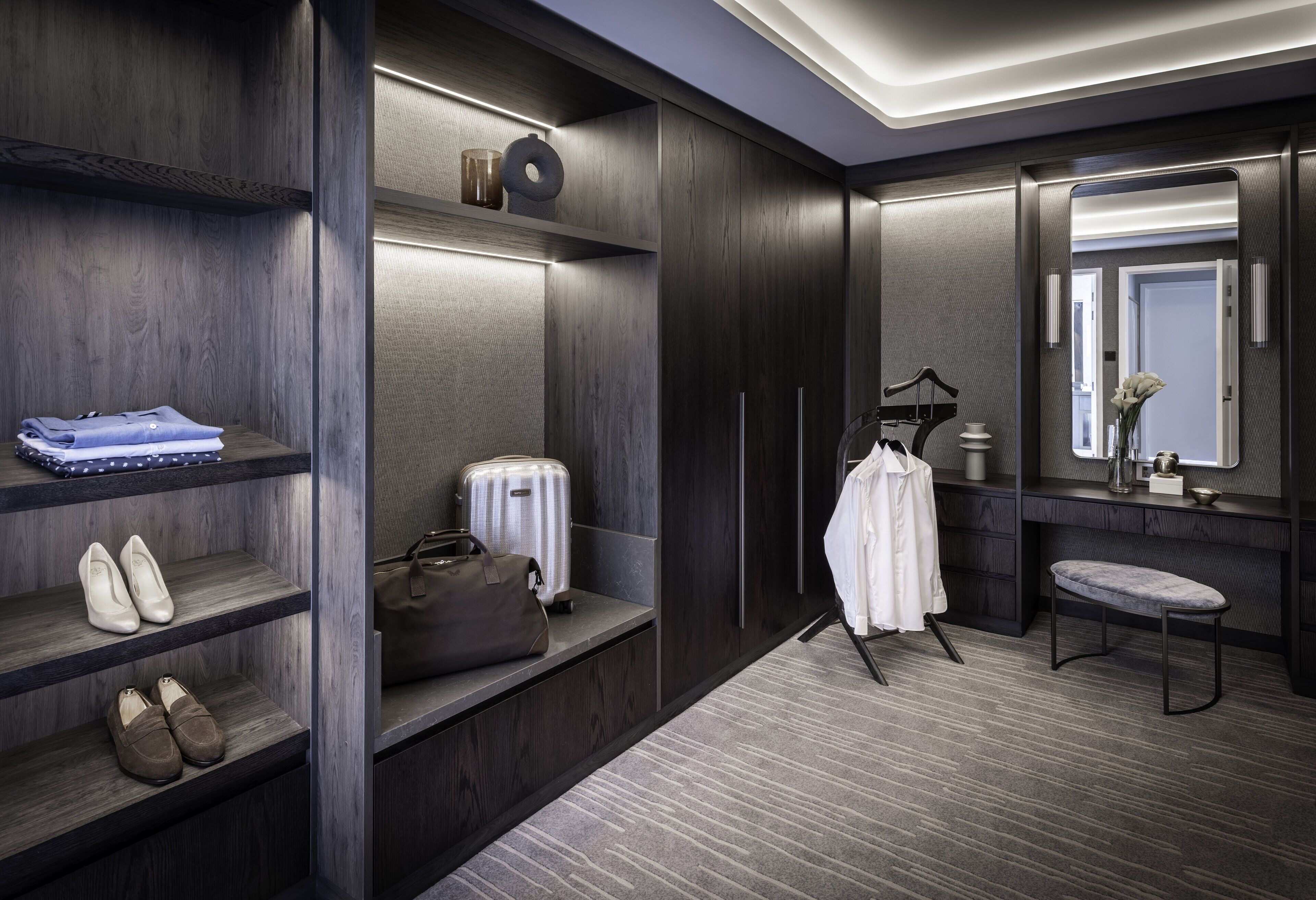 A modern hotel room with built-in wardrobes, a vanity with a mirror, and a seating area.